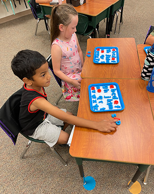 Two young students with magnetic letter boards sitting at desks