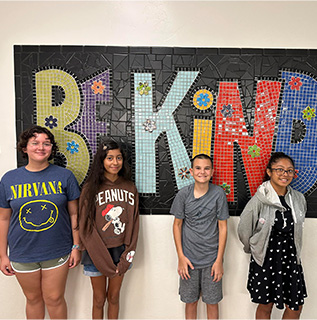 Students standing in front of a sign that reads Be Kind